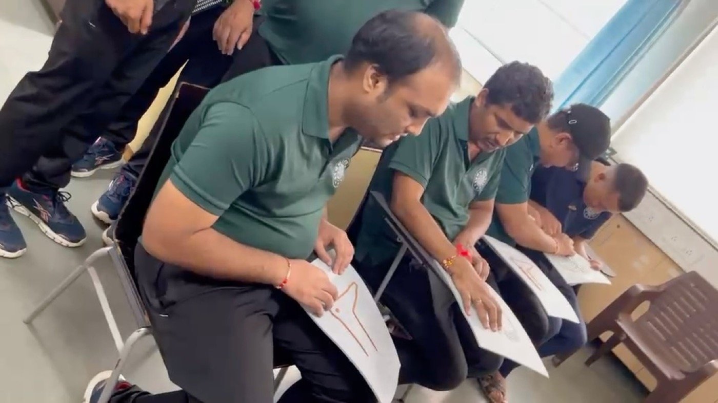 Four learners in Blind Relief Association polo shirts sitting in a row, each reading a raised-relief tactile diagram resting on their lap.